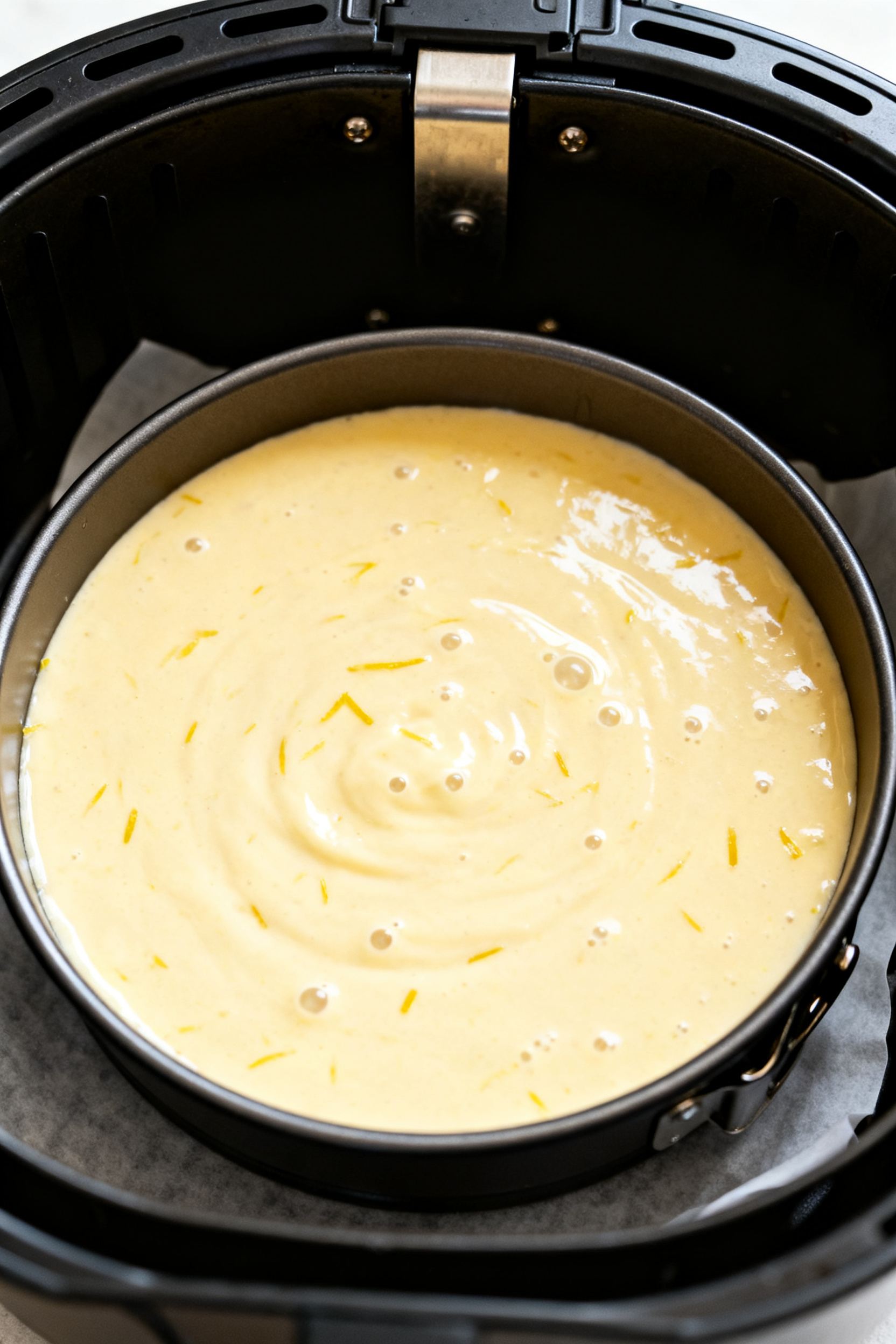Cooking process close-up: A 6-inch round pan of lemon drizzle cake batter just placed in an air frye