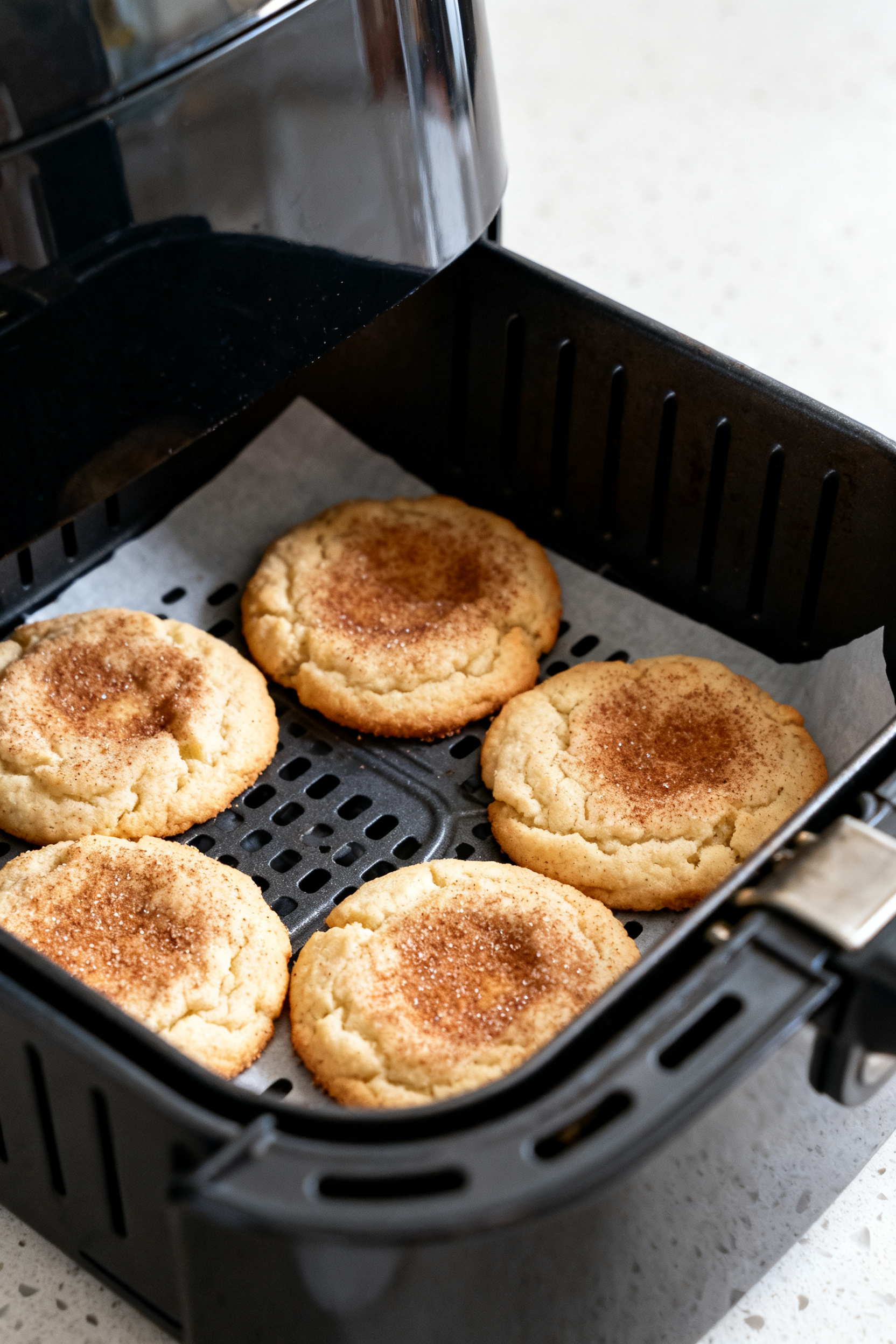 Close-up detail: Freshly air-fried snickerdoodles resting in the open air fryer basket, puffed with