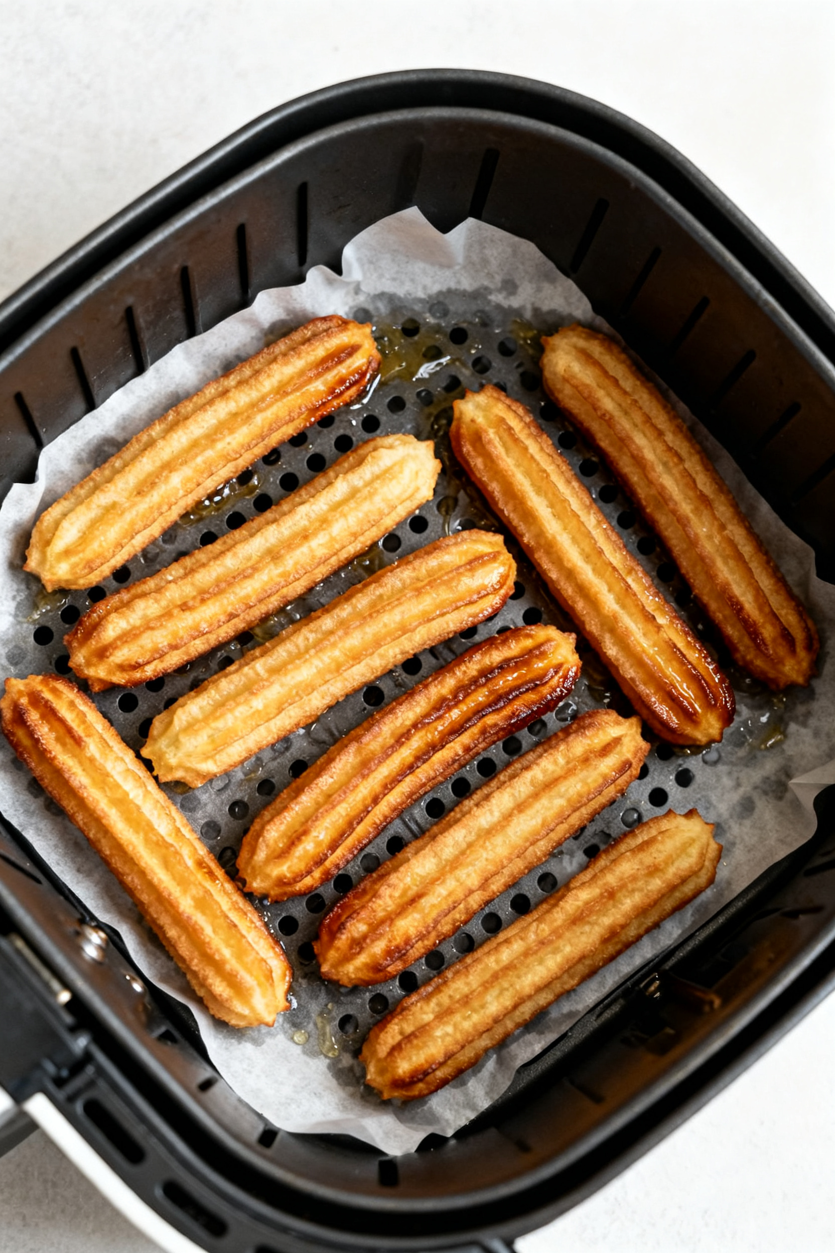 Cooking process: Overhead shot of an air fryer basket lined with perforated parchment, a single laye